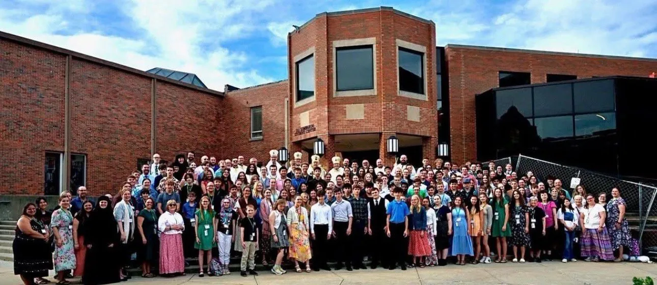 A large group photo of Byzantine Catholic teens, clergy, and bishops gathered outside a university building