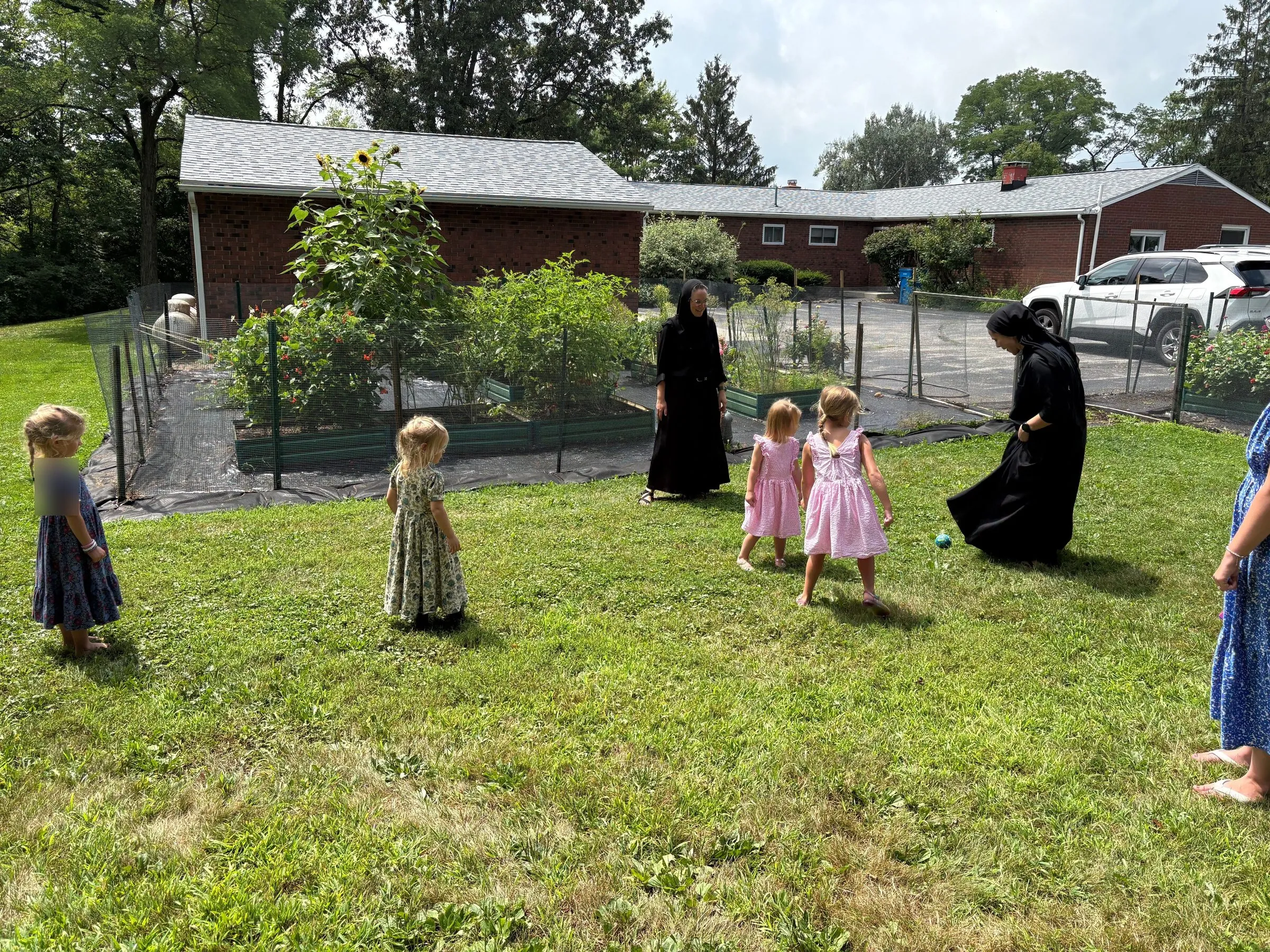 Two monastic sisters in black playing soccer with young girls on the monastery lawn