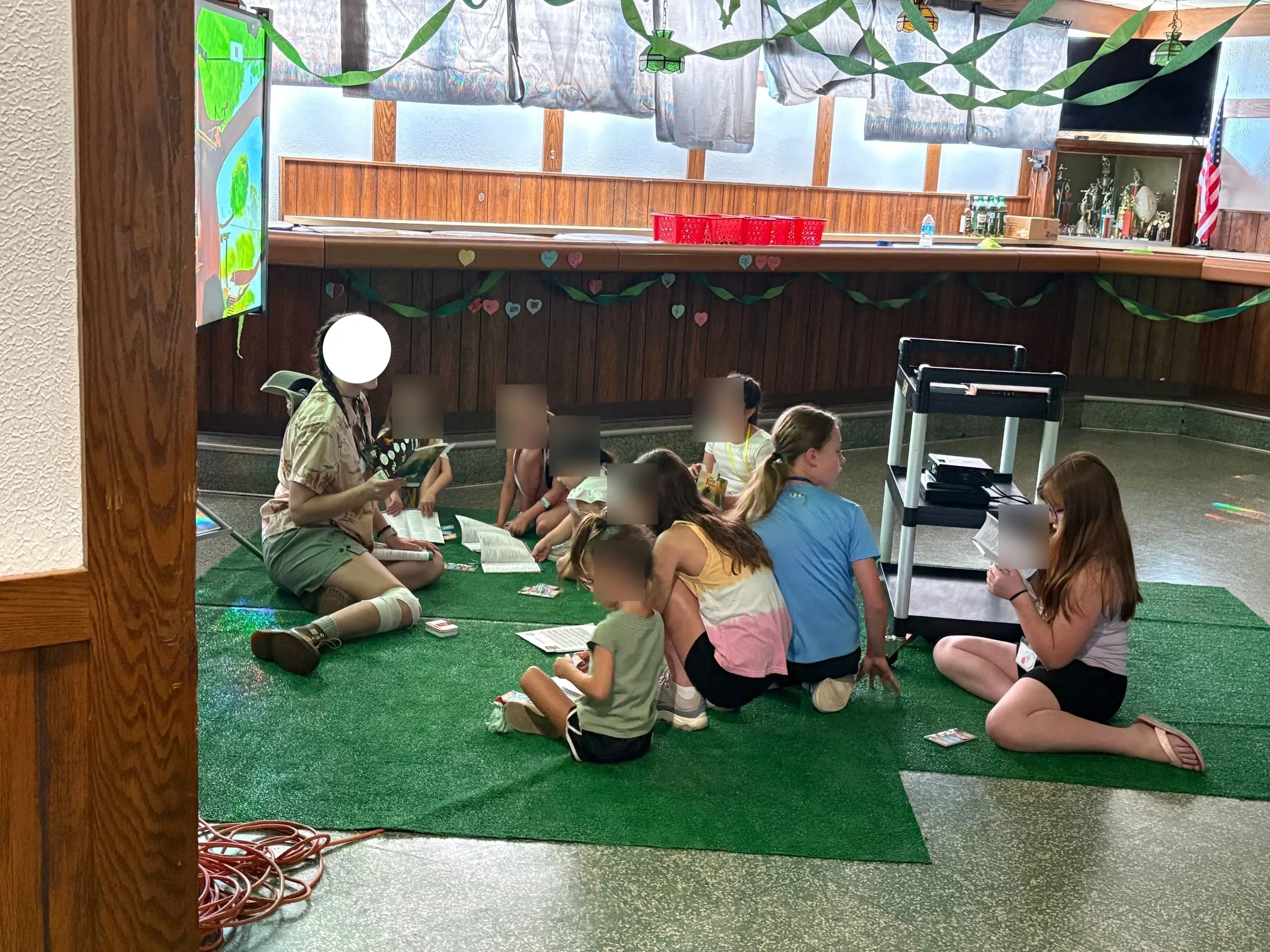 A leader reading to a circle of children seated on green mats